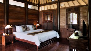 A wooden room with a large bed, nightstands, a mirror, and a television. - Sea Breeze Candidasa (Manggis)