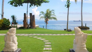 A pathway leading to a view of the ocean, flanked by two statues and palm trees. - Sea Breeze Candidasa (Manggis)