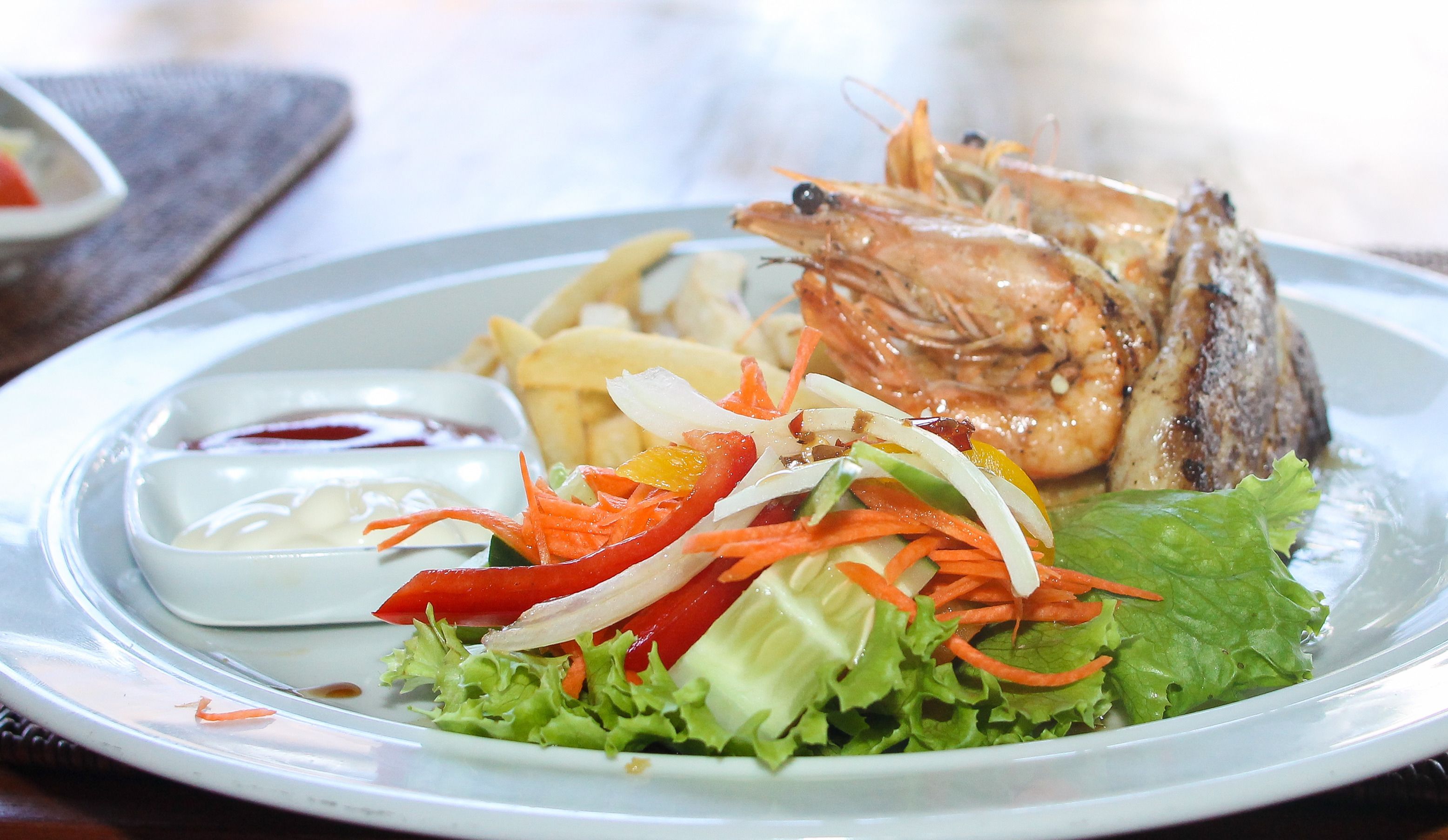 A plate with grilled shrimp, a salad, and a small bowl of sauce.
