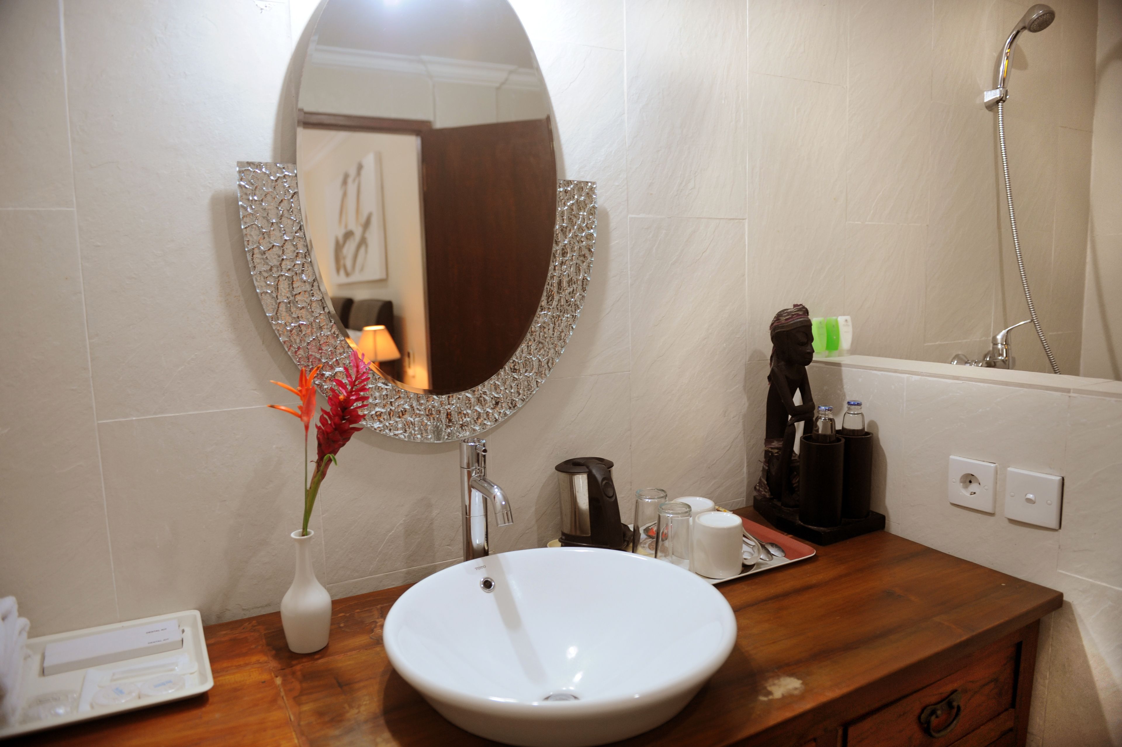 Une salle de bain avec un lavabo blanc, un miroir rond doté d’un cadre décoratif, une douche et un meuble-lavabo en bois.