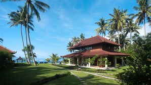 A resort with a large building, palm trees, and a clear blue sky. - Sea Breeze Candidasa (Manggis)