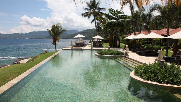 A pool with a view of the sea and mountains, surrounded by palm trees and lounge chairs. - Sea Breeze Candidasa (Manggis)