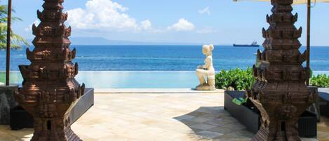 Area piscina con una statua, due ombrelloni e vista sull'oceano.