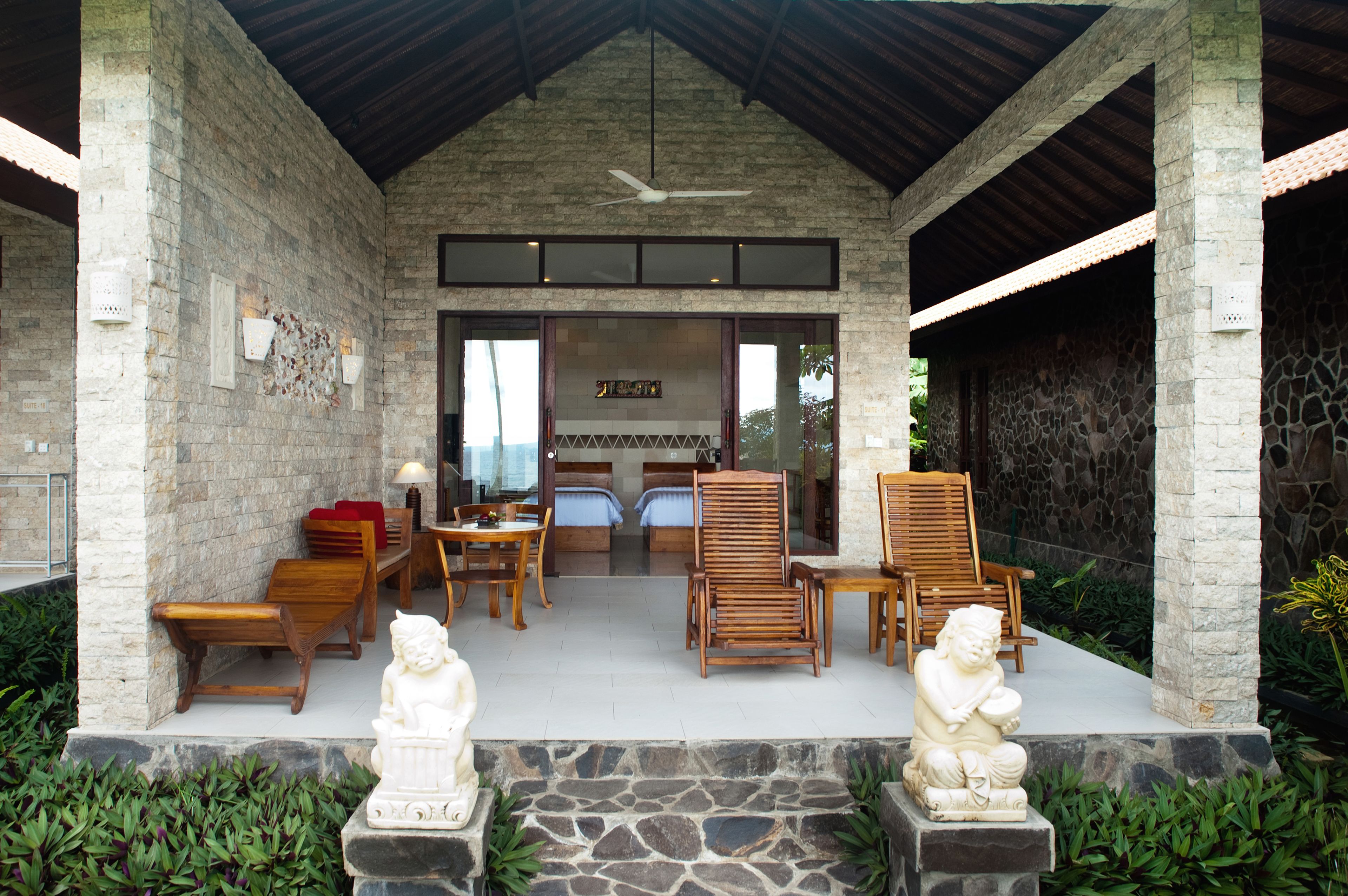 A covered outdoor seating area with stone walls, wooden furniture, and two stone statues.