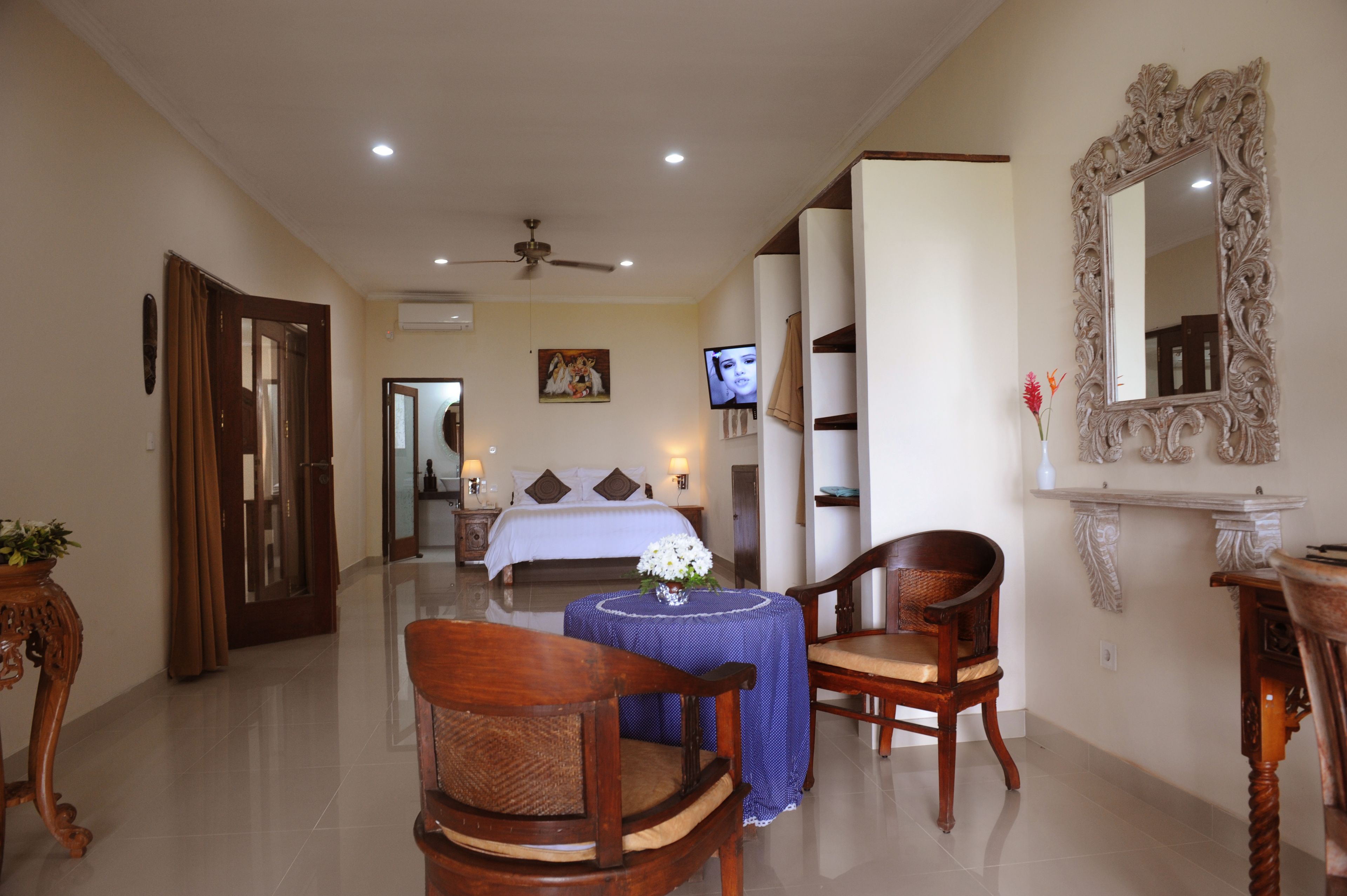 Habitación de hotel con cama, televisión, ventilador de techo, mesa de comedor con sillas y un espejo decorativo.