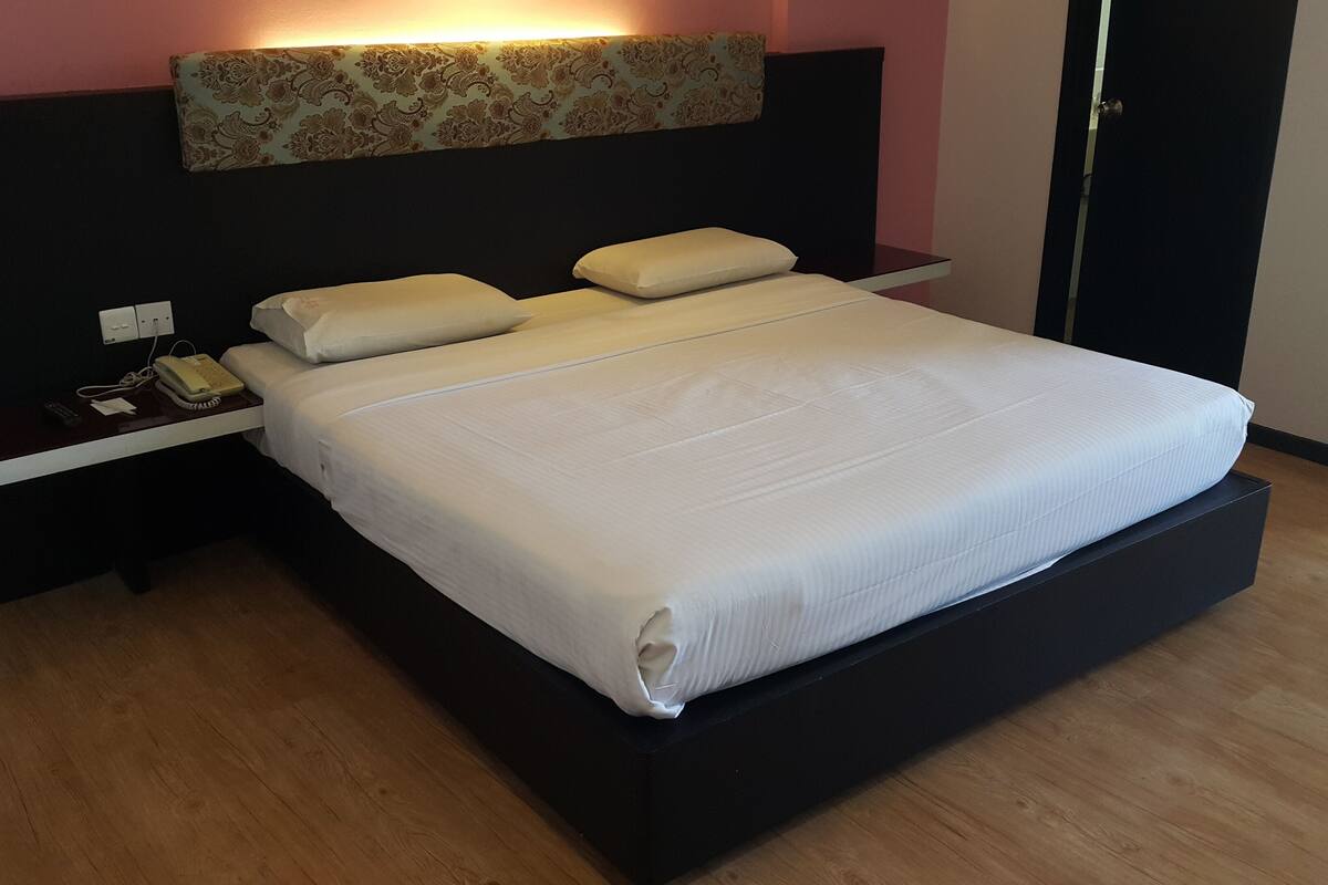 A modern hotel room with a large bed, a bedside table with a telephone, and a wall-mounted light fixture.