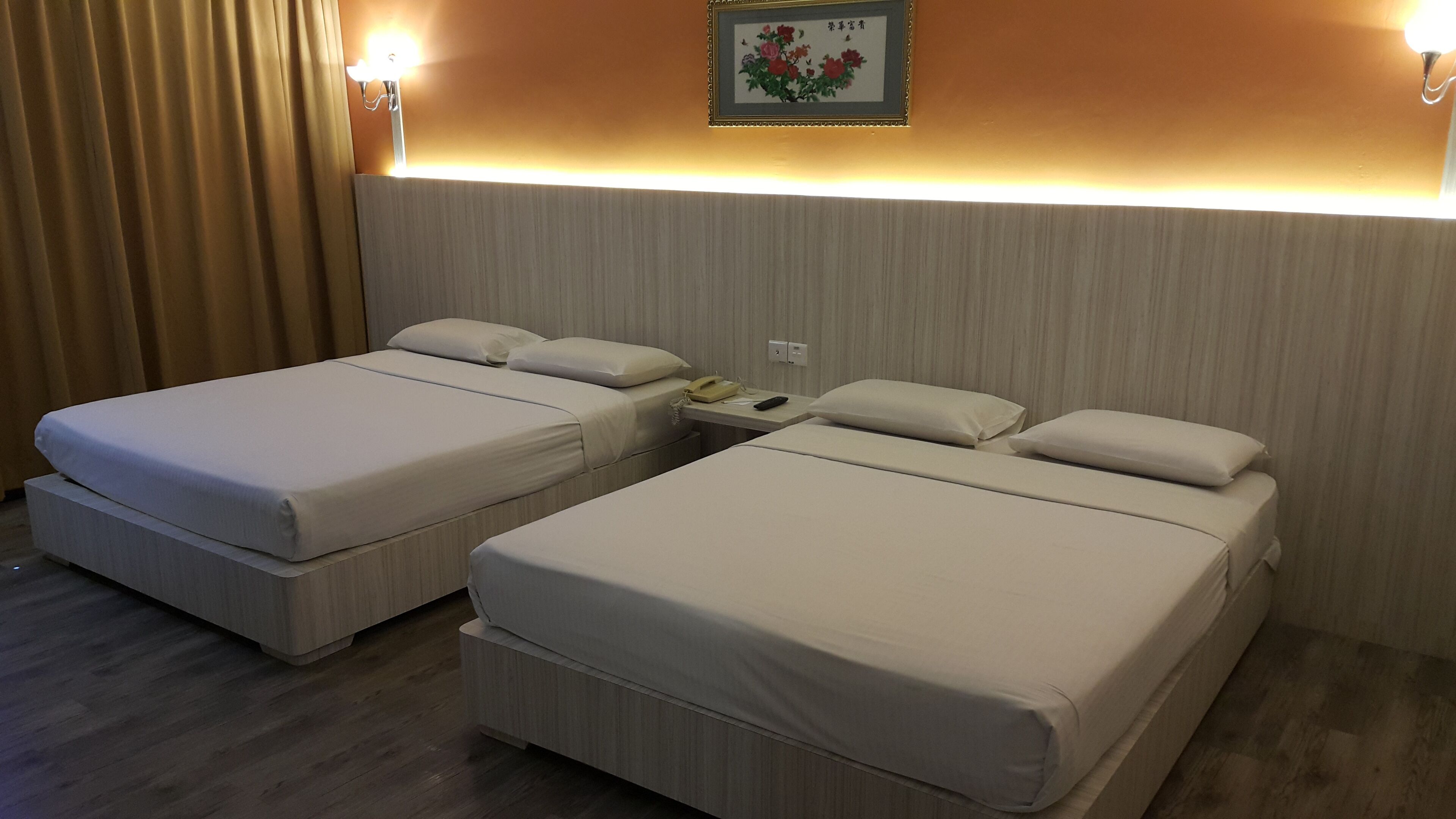 Habitación de hotel con dos camas, una mesita de noche con teléfono y control remoto, y una lámpara fijada a la pared.