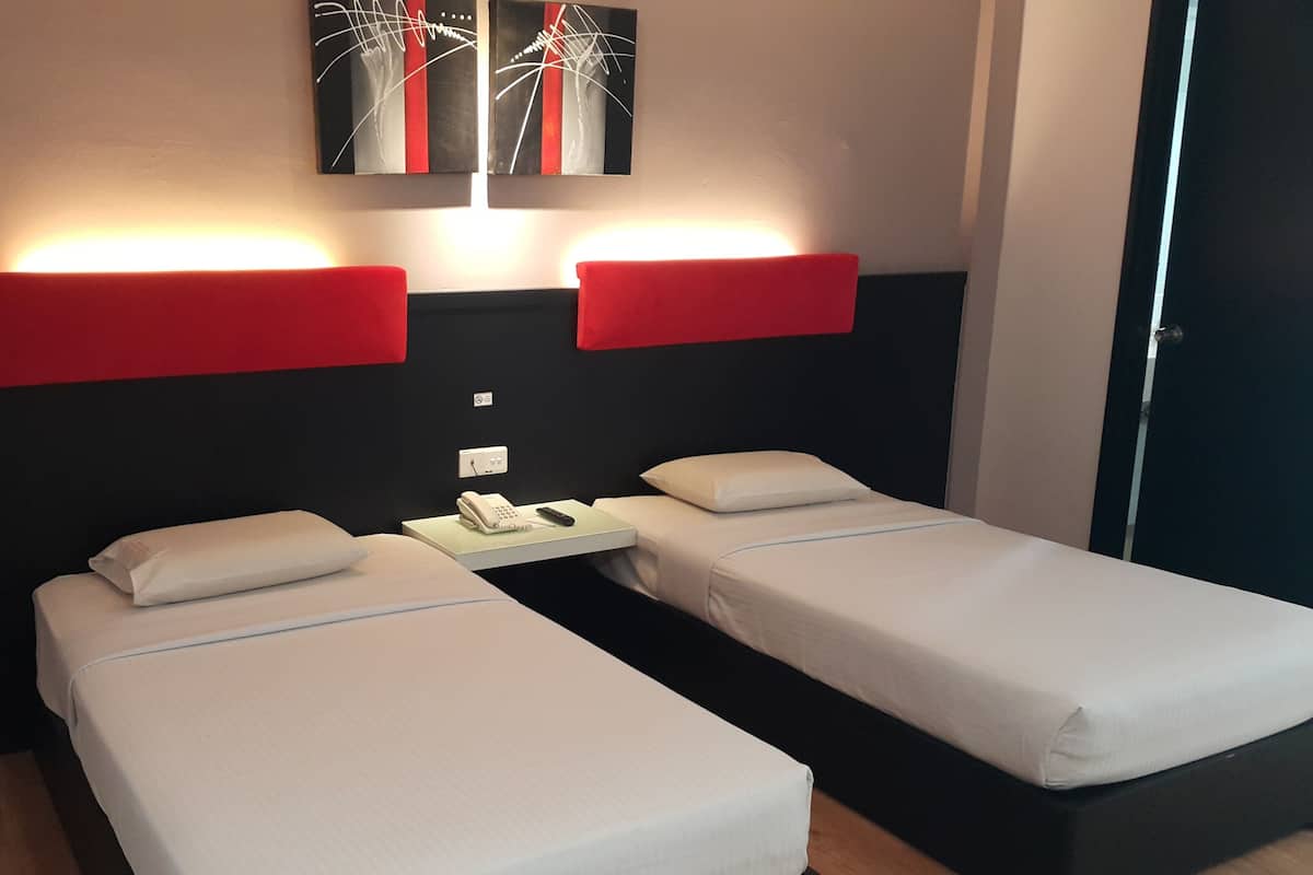 A hotel room with two single beds, a bedside table with a phone and remote, and red wall-mounted lights.