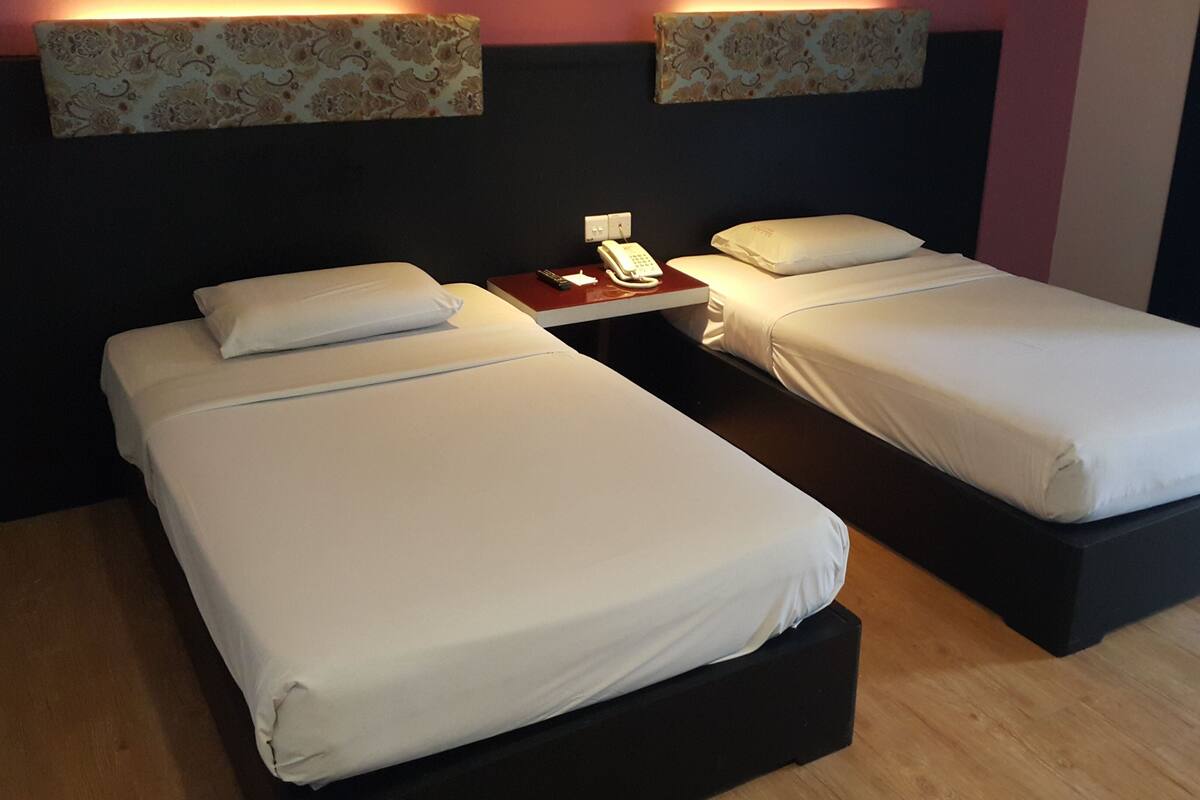 A hotel room with two beds, a bedside table with a phone, and a wall-mounted light fixture.