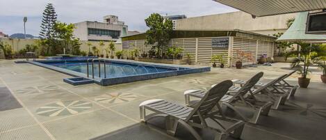 Un área de piscina en la azotea con sillas de descanso y plantas en macetas.