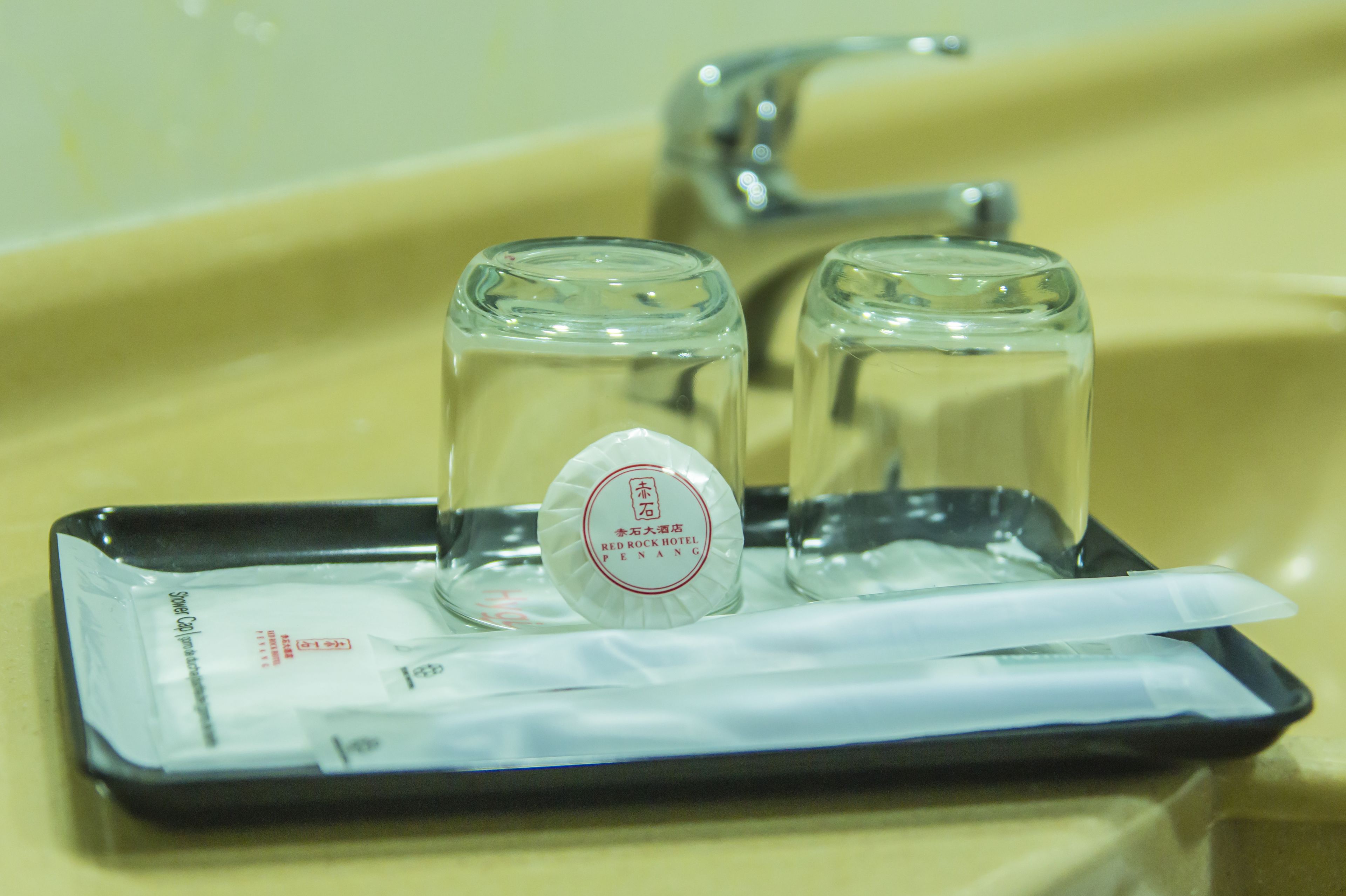 A tray with two glasses and a bottle of Red Rock Hotel Penang branded water, placed on a yellow sink.