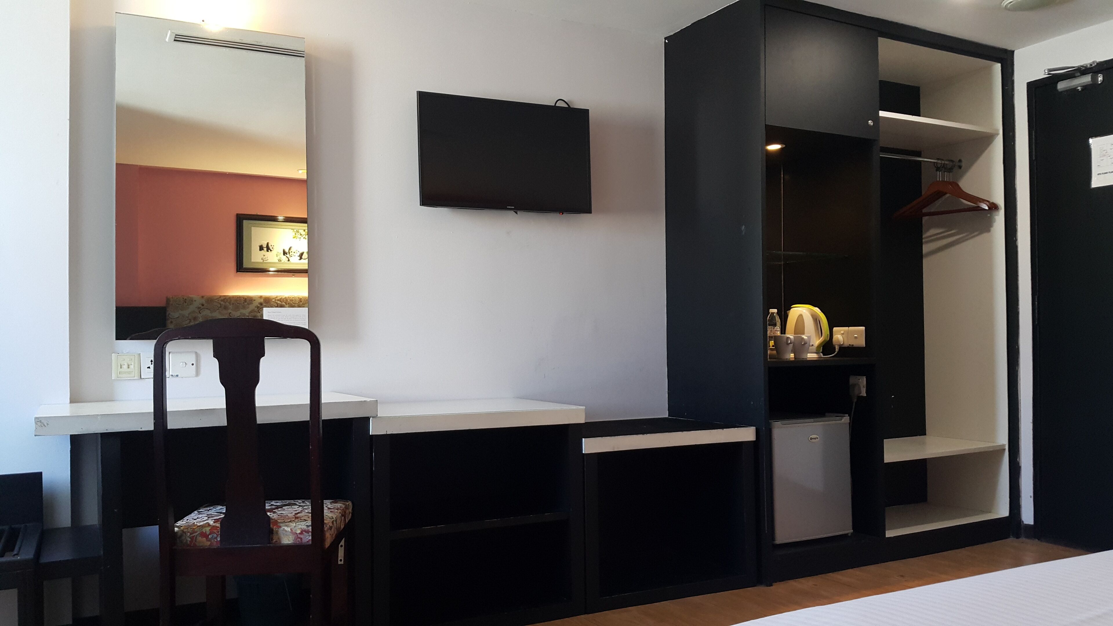 Een kleine kamer met een bureau, stoel en een garderobe met spiegel.