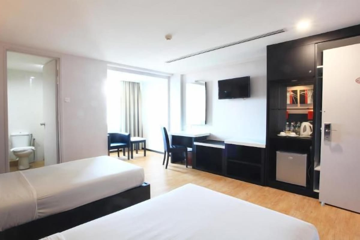 Habitación de hotel con cama, escritorio, silla, televisor y kitchenette.