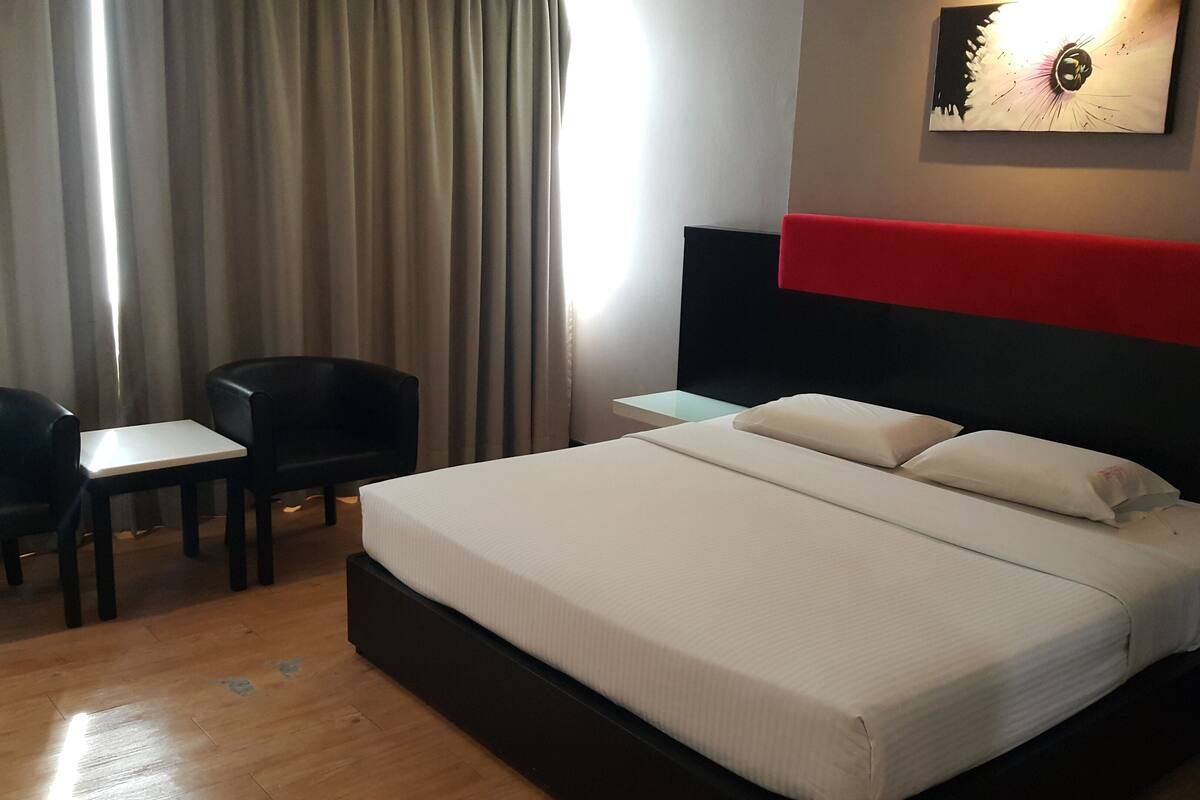 A hotel room with a bed, two chairs, a small table, a nightstand, and a wall-mounted artwork.
