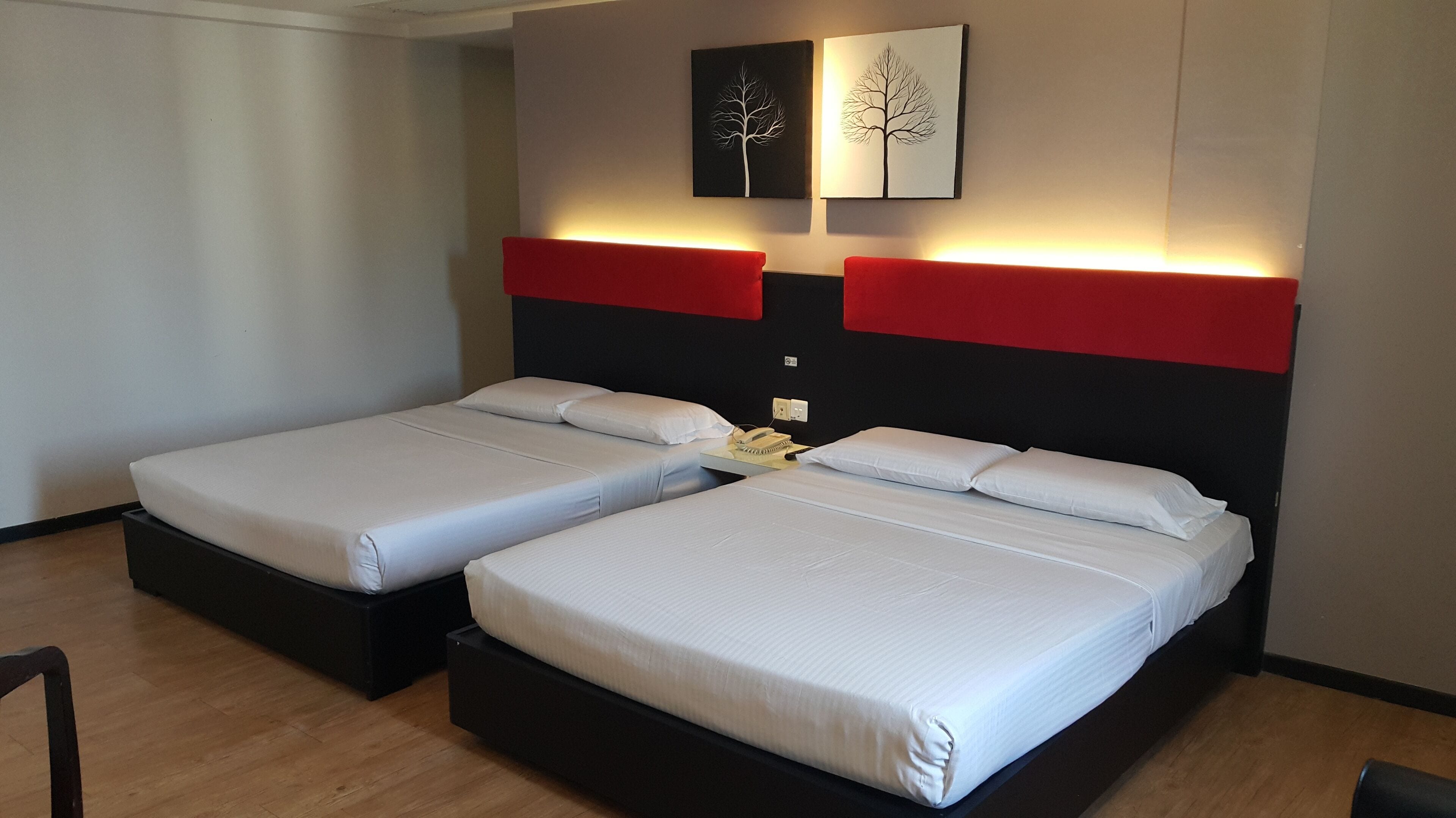 A hotel room with two beds, a red accent wall, and two wall-mounted artworks.