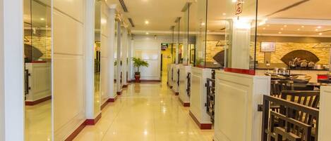 A hotel corridor with a shiny tiled floor, glass doors, and a reception area with a counter and chairs.