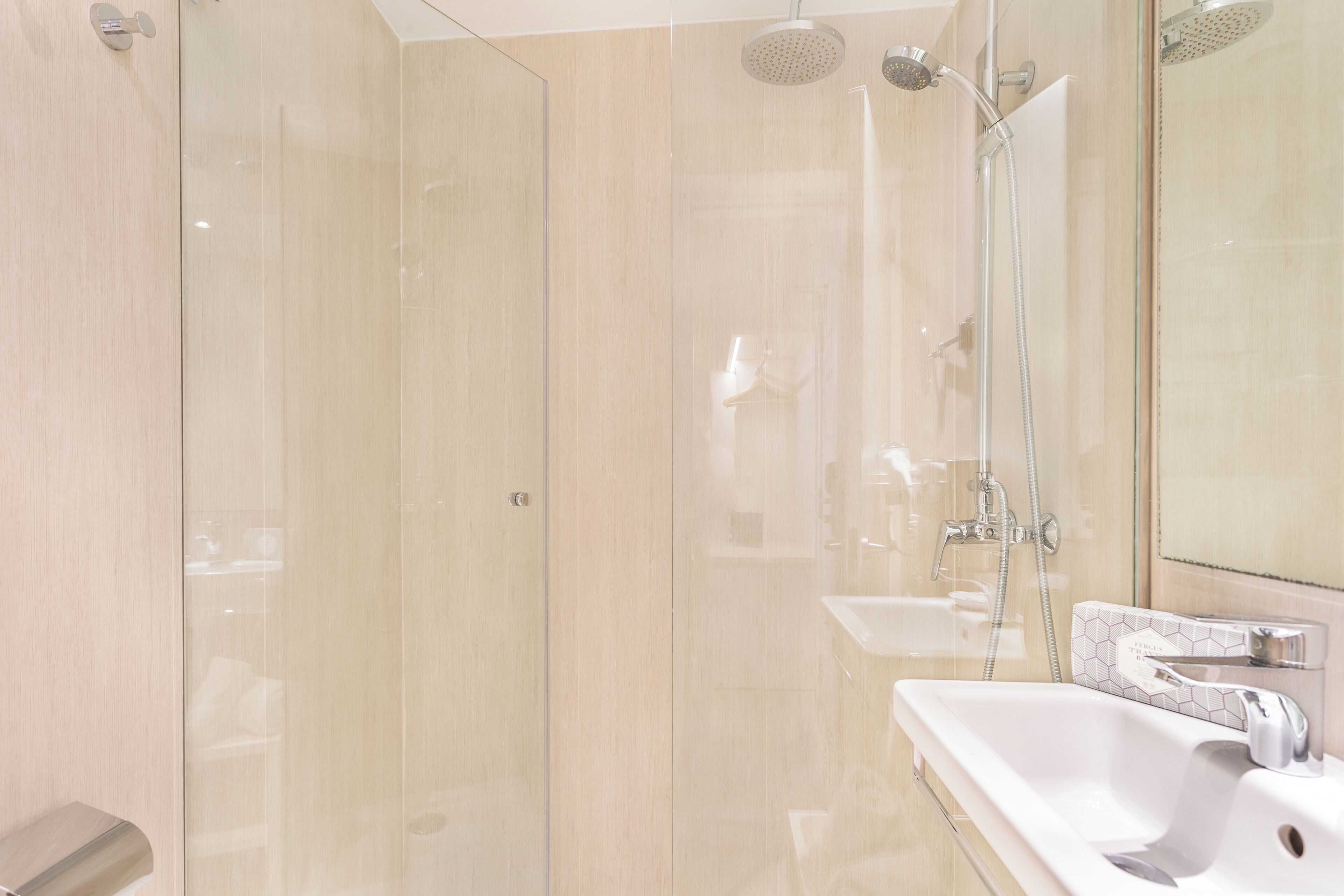 Un baño moderno con ducha envuelta en vidrio, un lavabo blanco y un espejo grande.