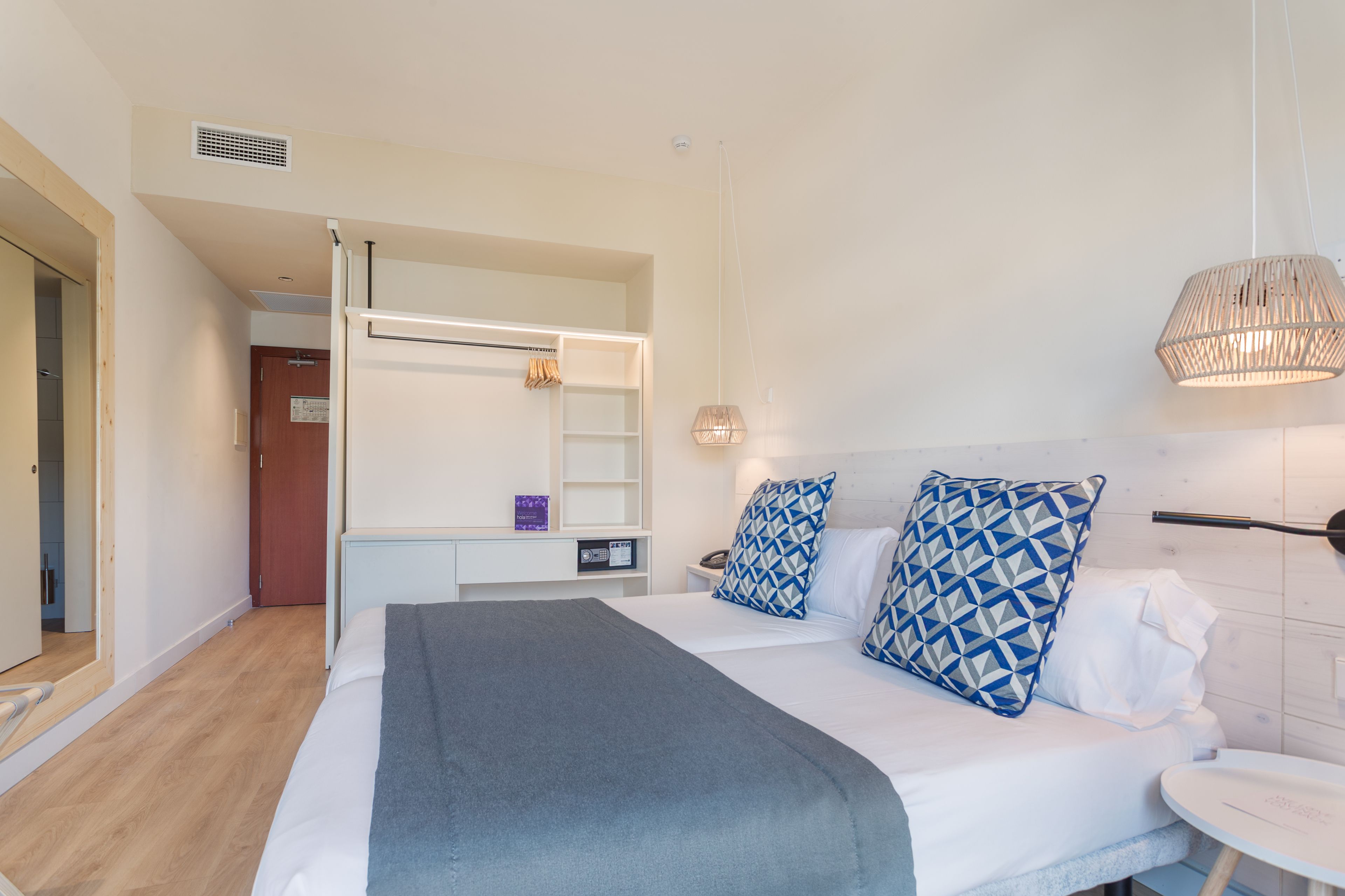 Une chambre d’hôtel moderne avec un grand lit, des tables de chevet, un bureau et un luminaire suspendu.