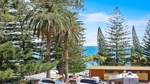 A parking area with several cars, a building with a brown roof, and a view of the ocean. - Seabreeze Beach Hotel (South West Rocks)