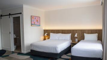 Habitación de hotel con dos camas, cabecero de madera, alfombra abstracta de colores y una puerta que da al baño.
