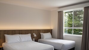 A hotel room with two beds, a nightstand, a lamp, and a window with curtains. - Seabreeze Beach Hotel (South West Rocks)