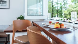 A dining area with a wooden table, chairs, and a view of trees through a window. - Seabreeze Beach Hotel (South West Rocks)