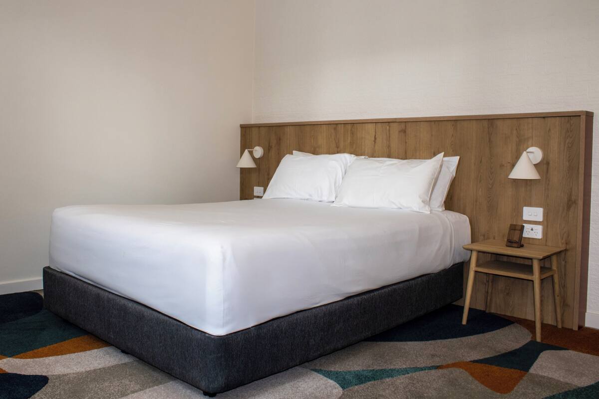 A neatly made bed with white linens, a wooden headboard, and two bedside lamps.