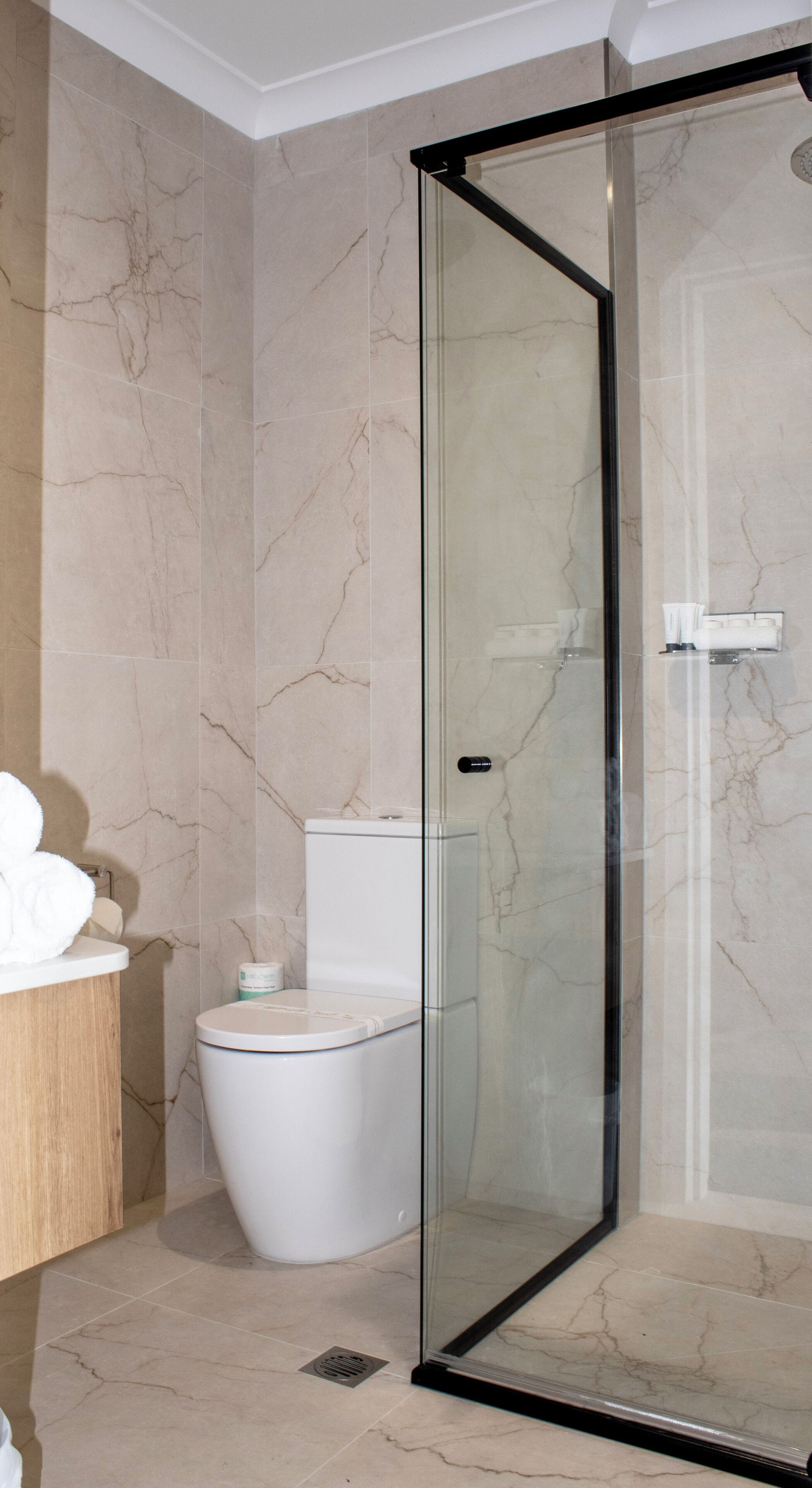 A bathroom with a glass-enclosed shower, a toilet, and a sink with a towel.