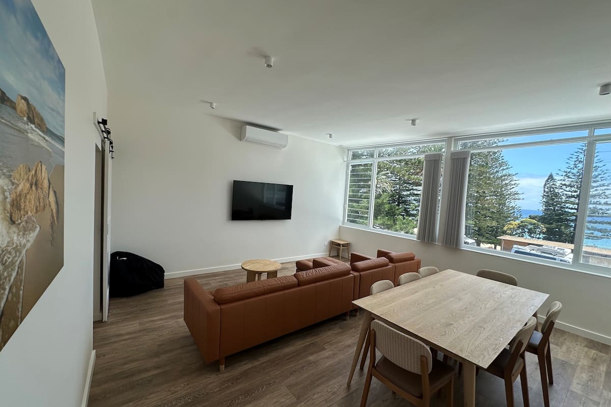 A modern living room with a sofa, a TV, a dining table, and a large window with a view.