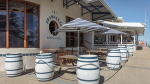 A beach hotel exterior with outdoor seating, large barrels, and a clear sky. - Seabreeze Beach Hotel (South West Rocks)