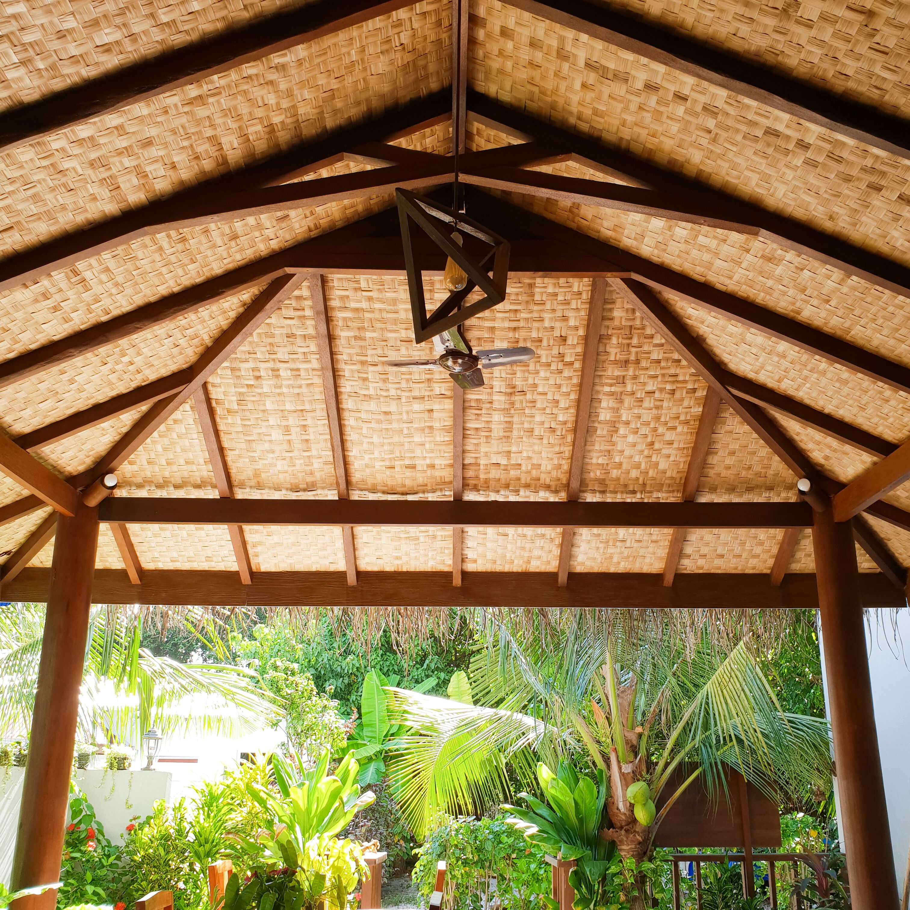 A covered outdoor area with a woven roof structure, wooden beams, and a hanging light fixture.
