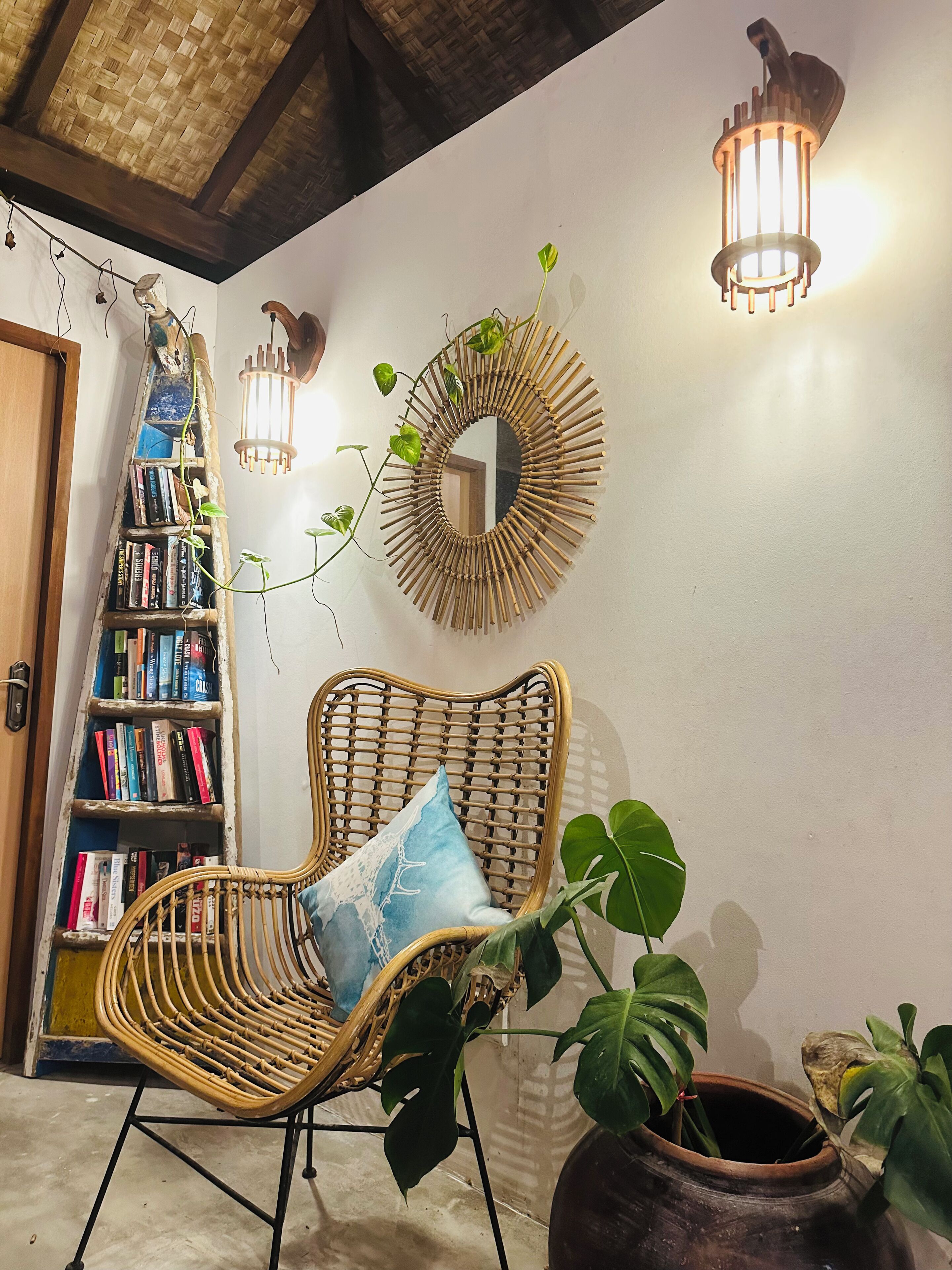 A room with a wicker chair, a bookshelf, a mirror, and two wall-mounted lights.
