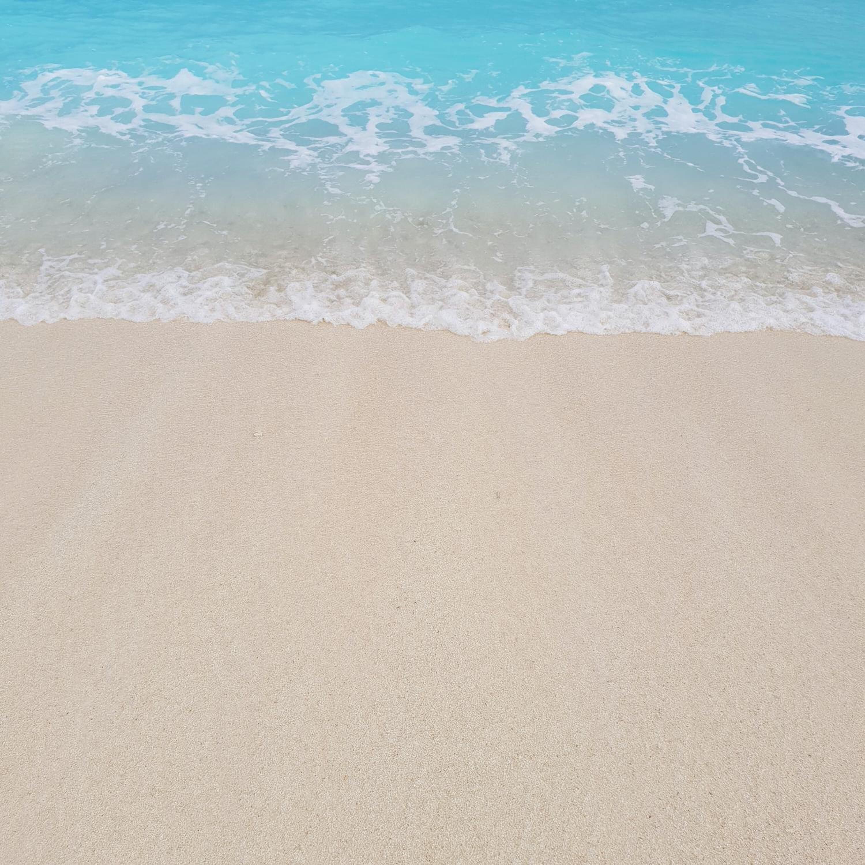 A beach with clear turquoise water and white foam waves.