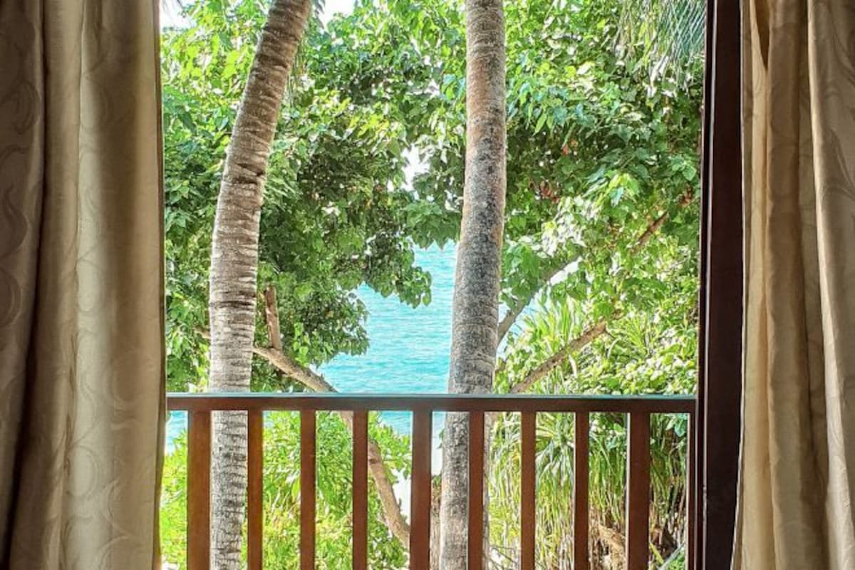 Un balcón con vistas a un paisaje tropical, que incluye palmeras y una masa de agua.