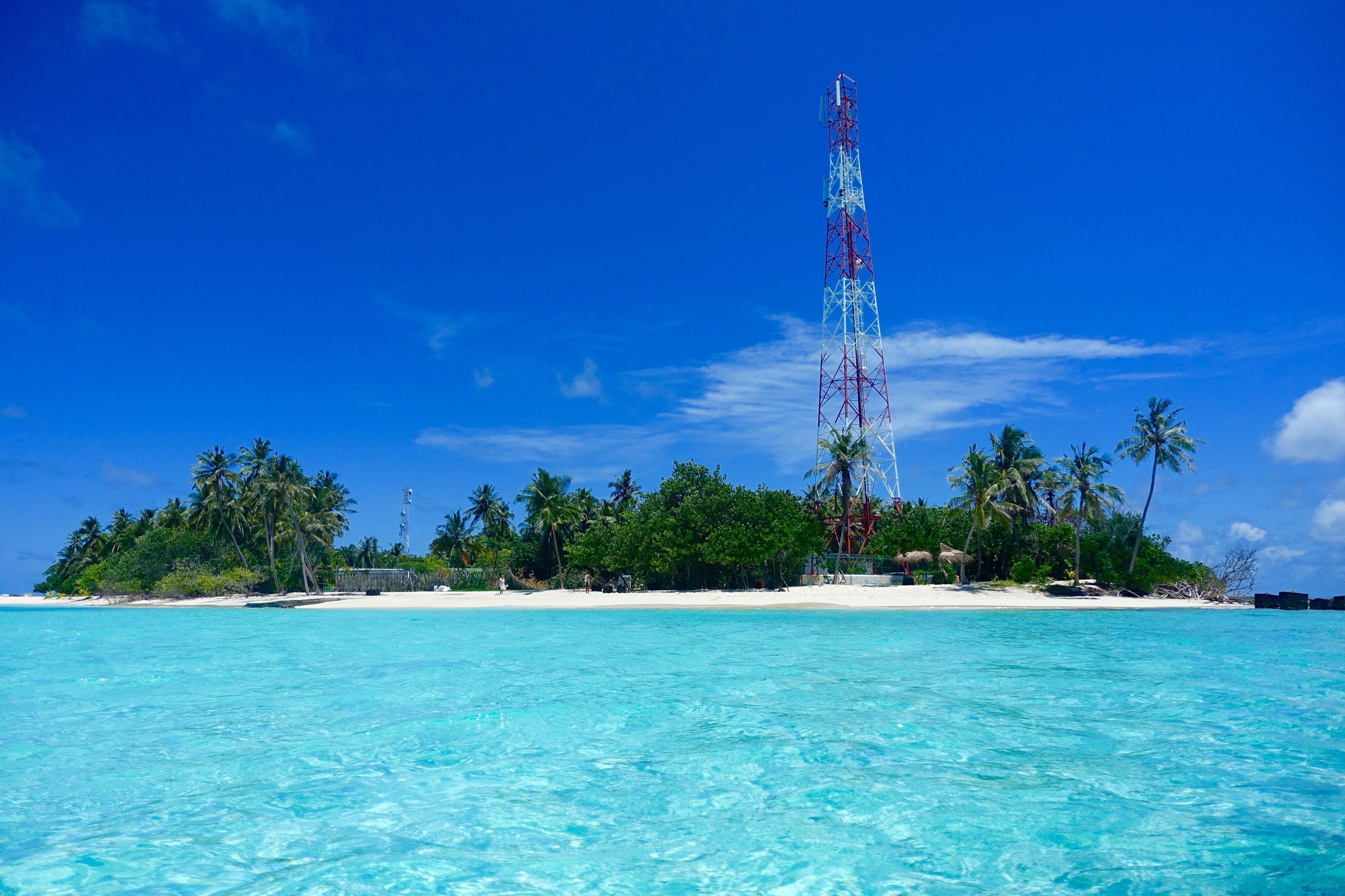 Ein Strand mit klarem türkisblauem Wasser, Palmen und einem hohen Funkturm.