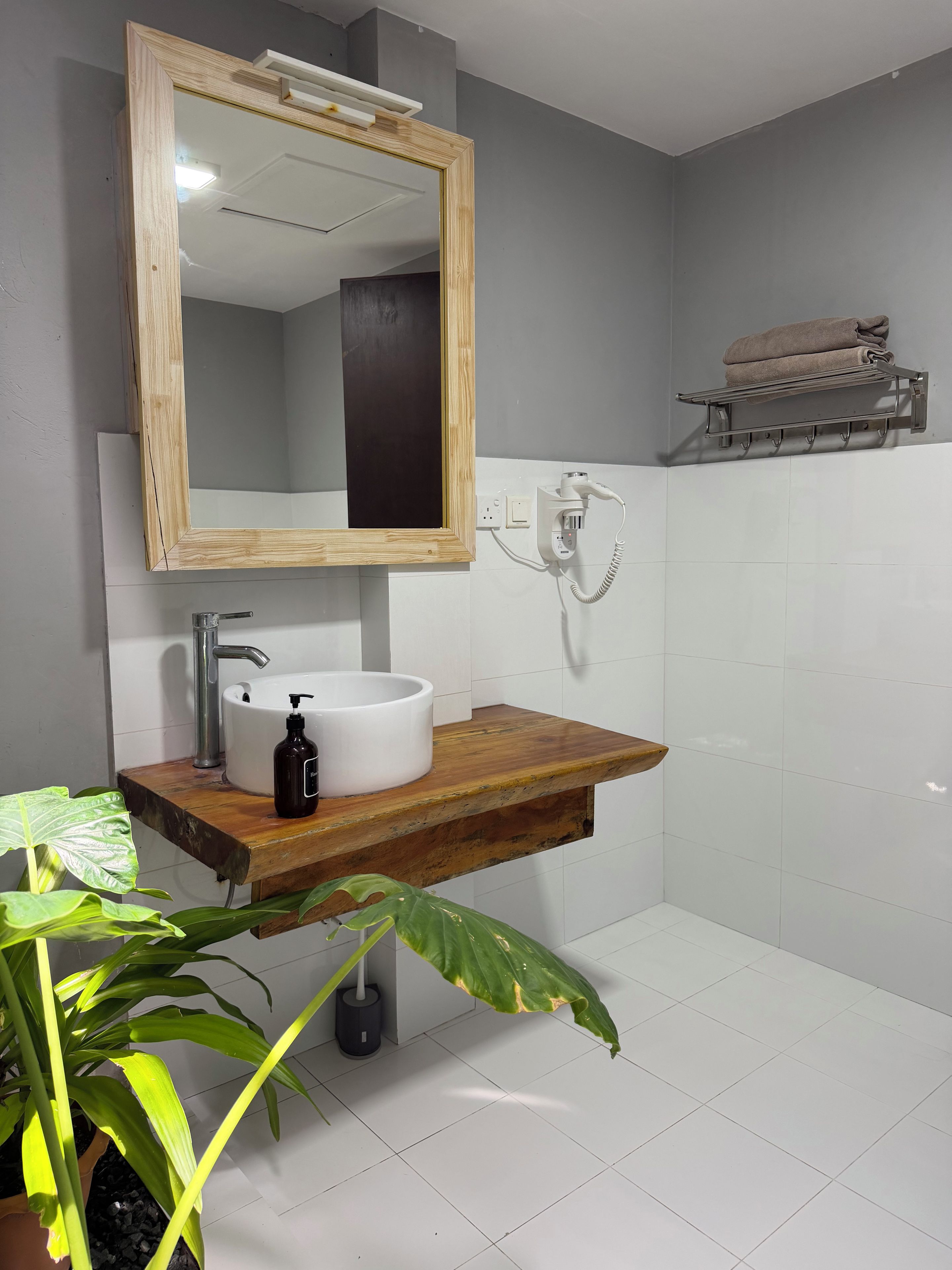 A bathroom with a wooden vanity, a white sink, a mirror, a towel rack, and a potted plant.