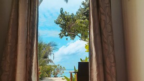 Una habitación con vista a la playa, a través de cortinas abiertas.