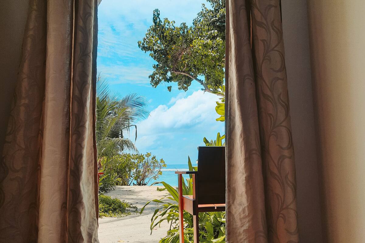 A room with a view of a beach through open curtains.