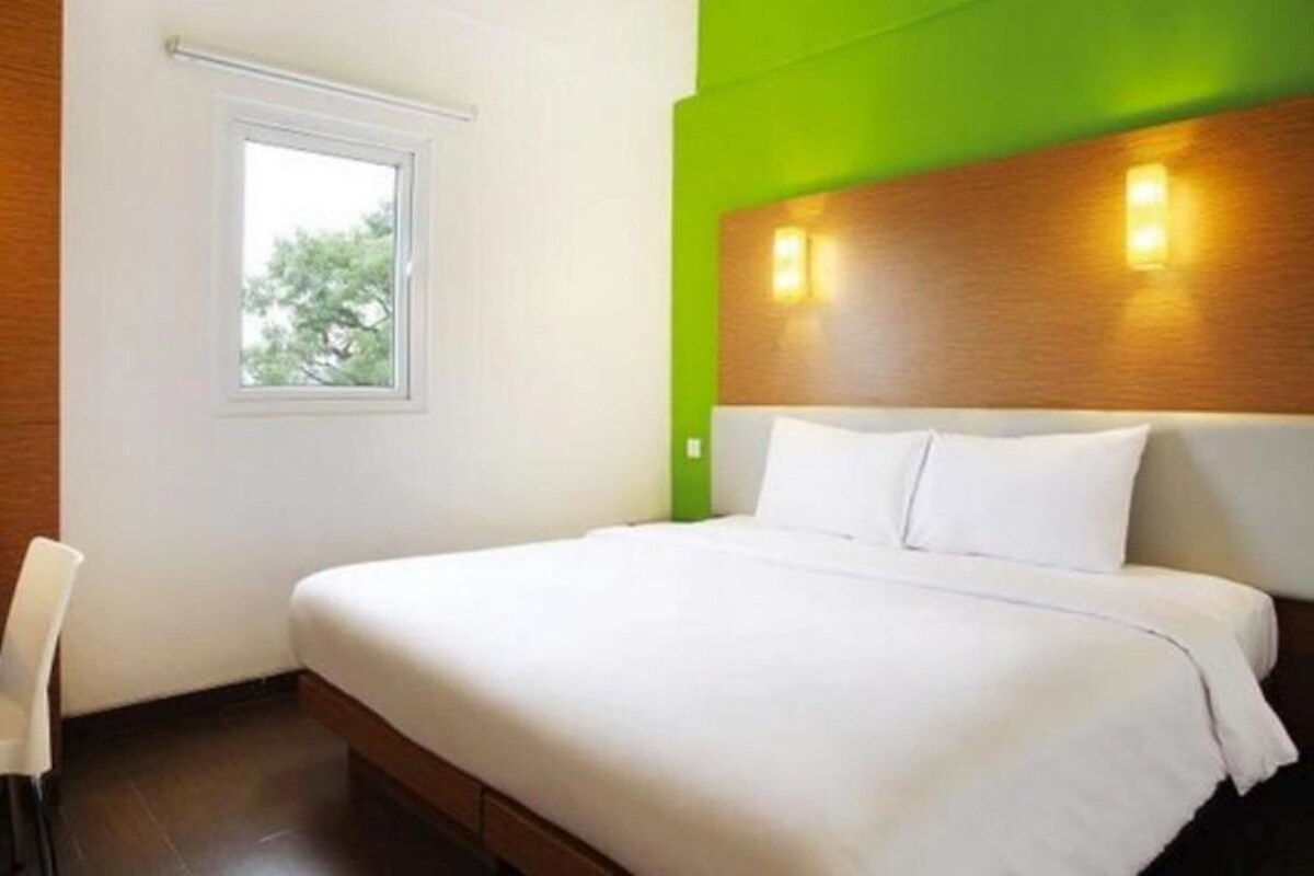 A hotel room with a bed, a window, and a green accent wall.