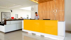 A hotel reception area with a bright yellow counter, a wooden accent wall, and a clock on the wall. - Amaris Hotel Sunset Road (Kuta)