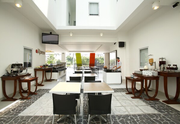 A spacious dining area with multiple tables and chairs, a kitchen counter, and a television mounted on the wall.