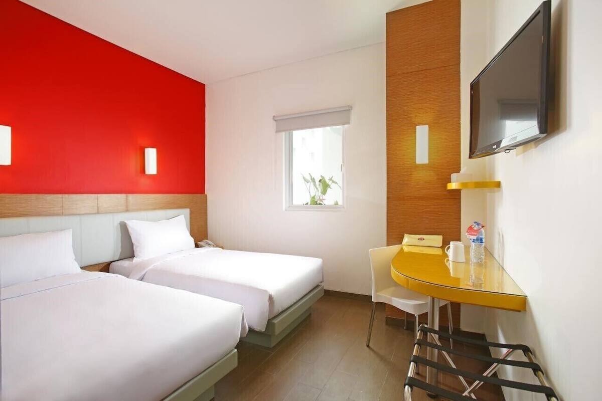 A hotel room with two beds, a desk, a chair, a TV, and a window.