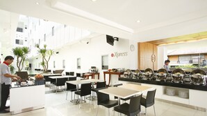A modern dining area with a buffet setup, including a variety of food containers and a seating arrangement with tables and chairs. - Amaris Hotel Sunset Road (Kuta)
