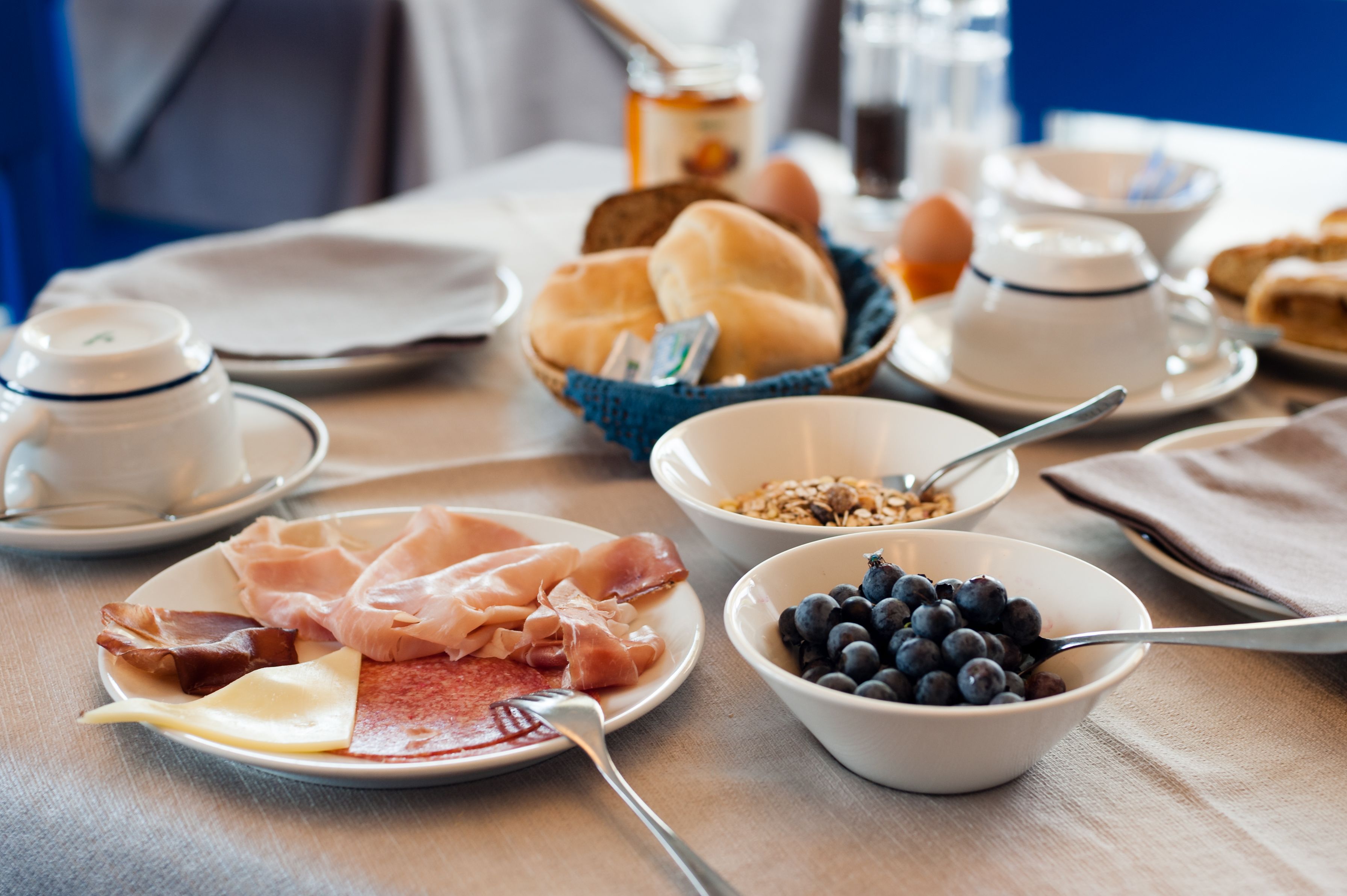 A breakfast table with various food items including meats, cheese, and fruits.