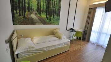 A modern room with a beige sofa, a desk, and a green chair. A large forest painting is on the wall.