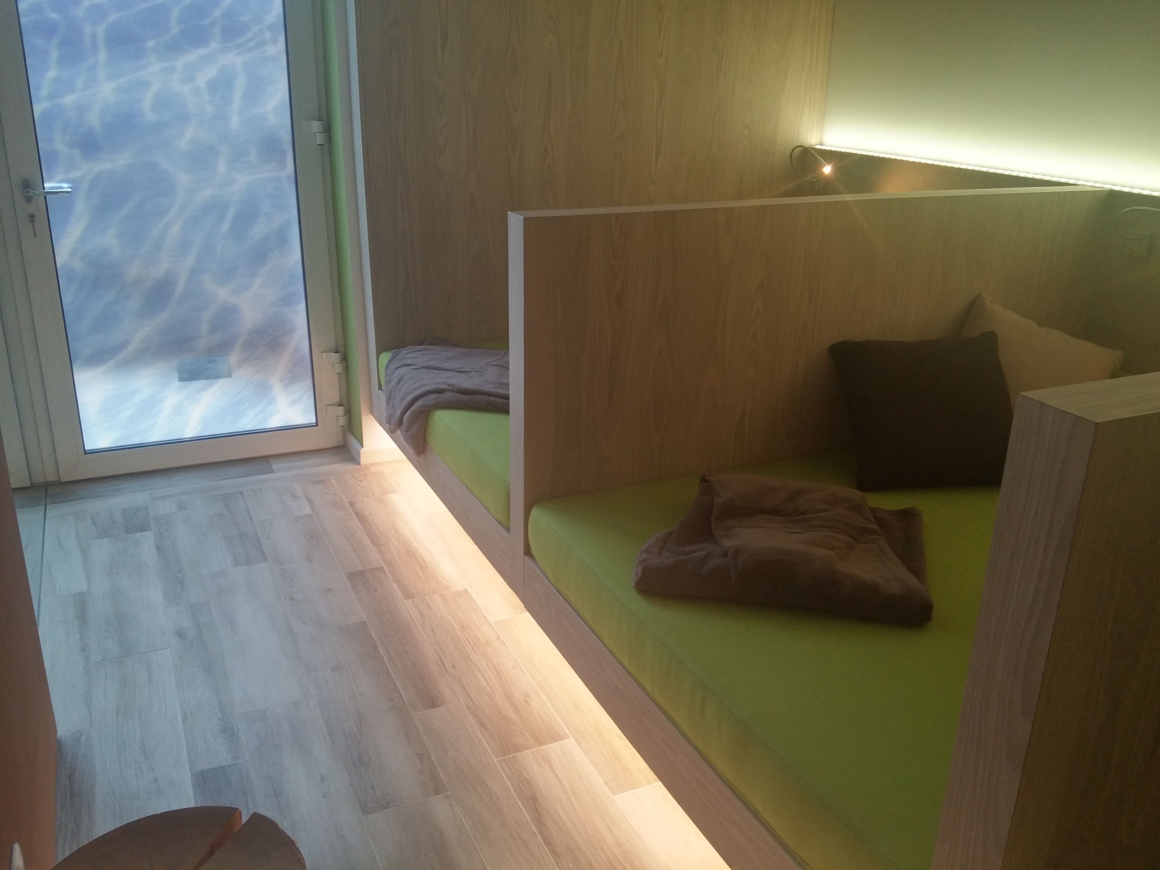 A modern room with a wooden floor, a green sofa, and a window with a view of the sky.