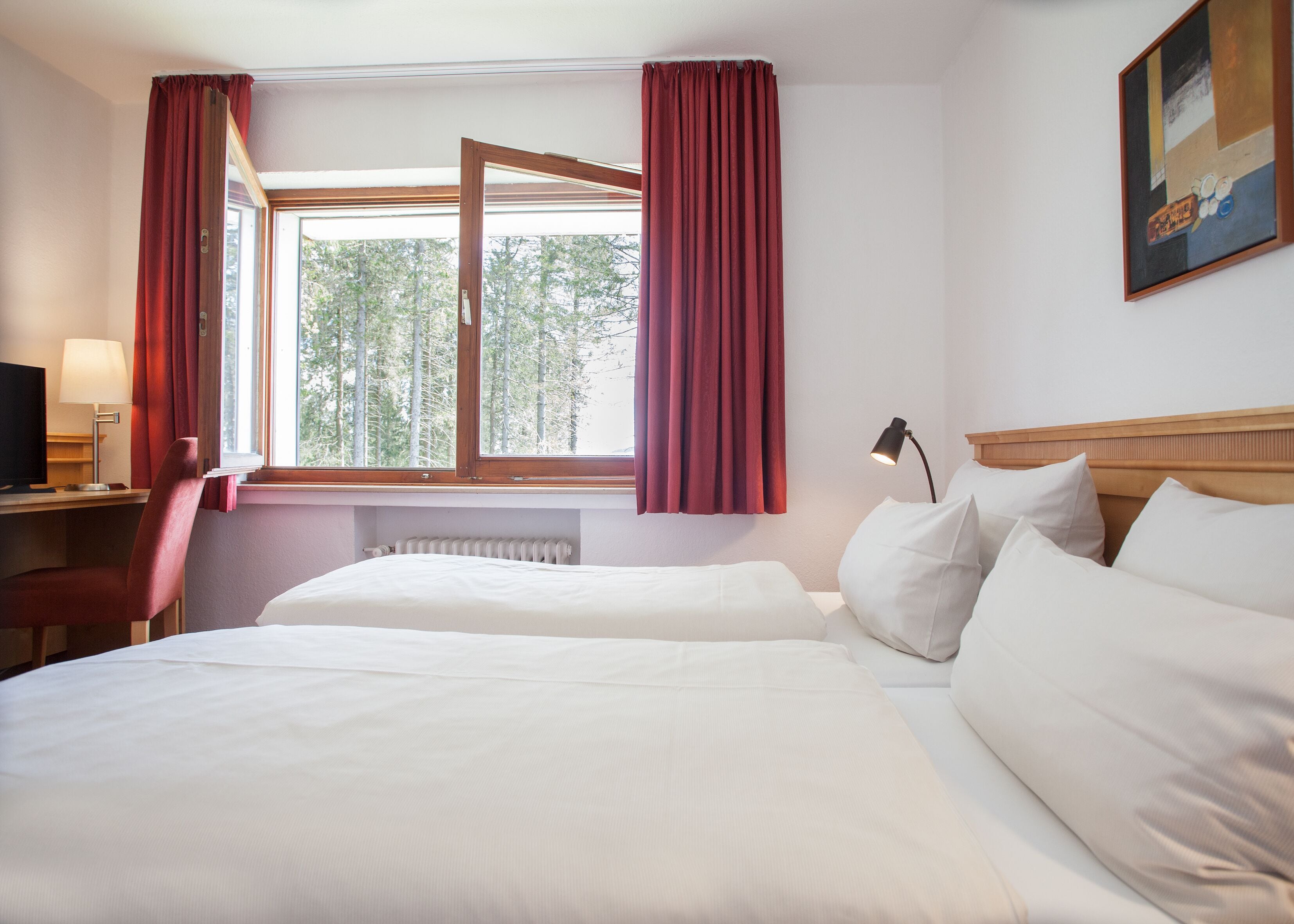 A hotel room with two beds, a desk with a lamp, a chair, and a window with curtains.