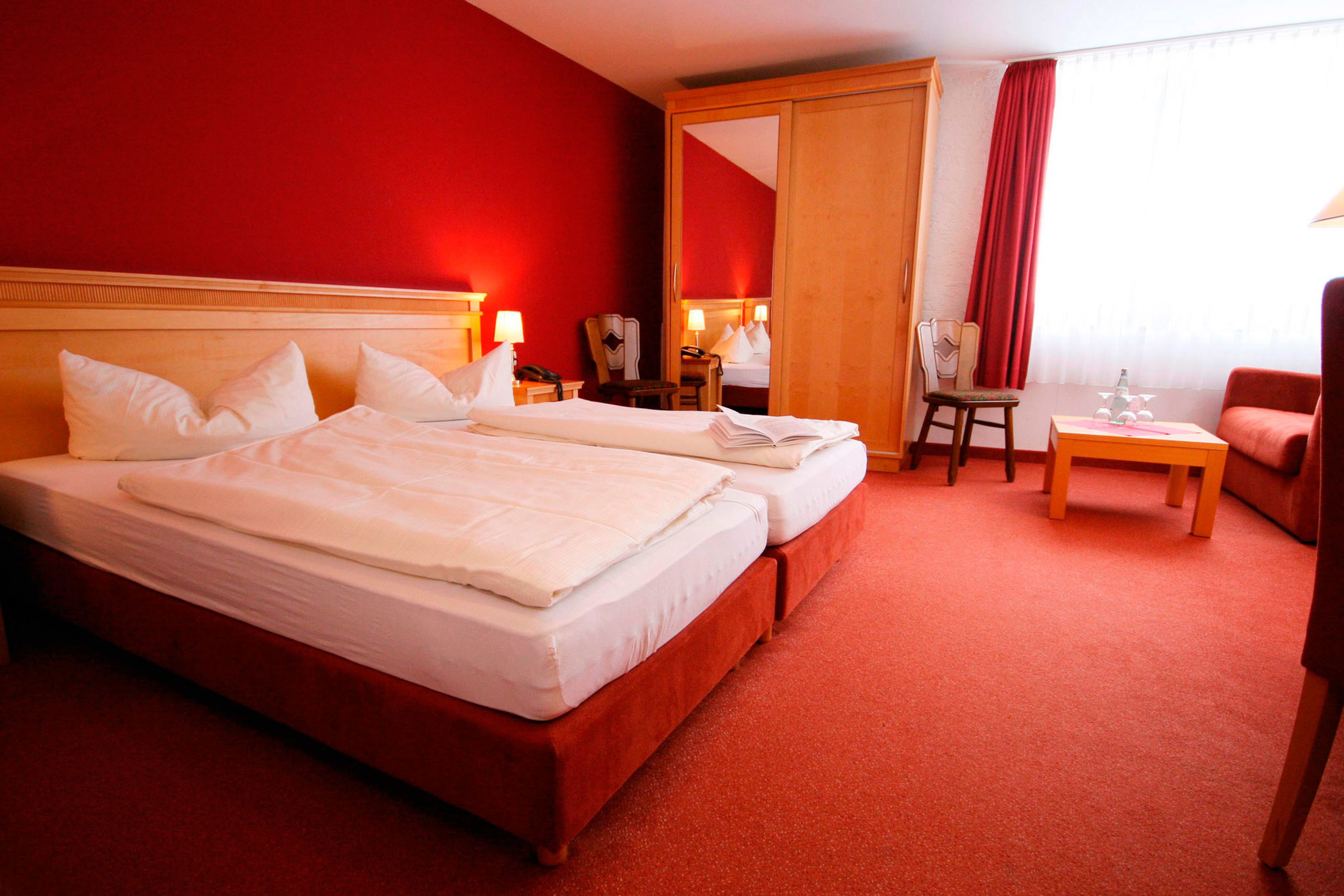A hotel room with two beds, a desk, a chair, and a red carpet.