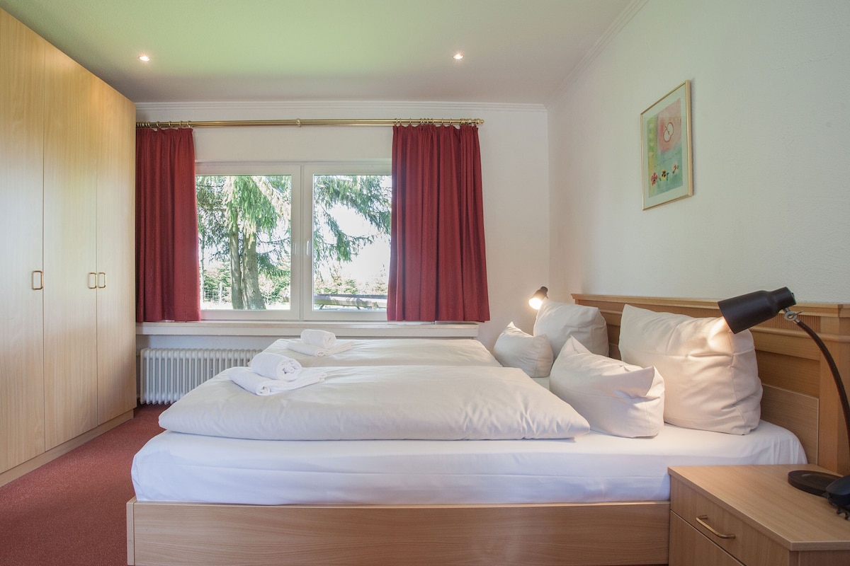 A neatly made bed with white linens, a bedside lamp, and a small bedside table with a phone.