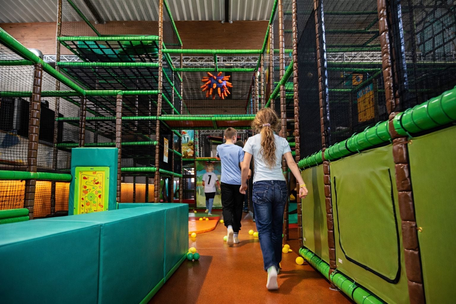 Zona de juegos interior con estructuras de escalada cubiertas por red y paredes acolchadas.